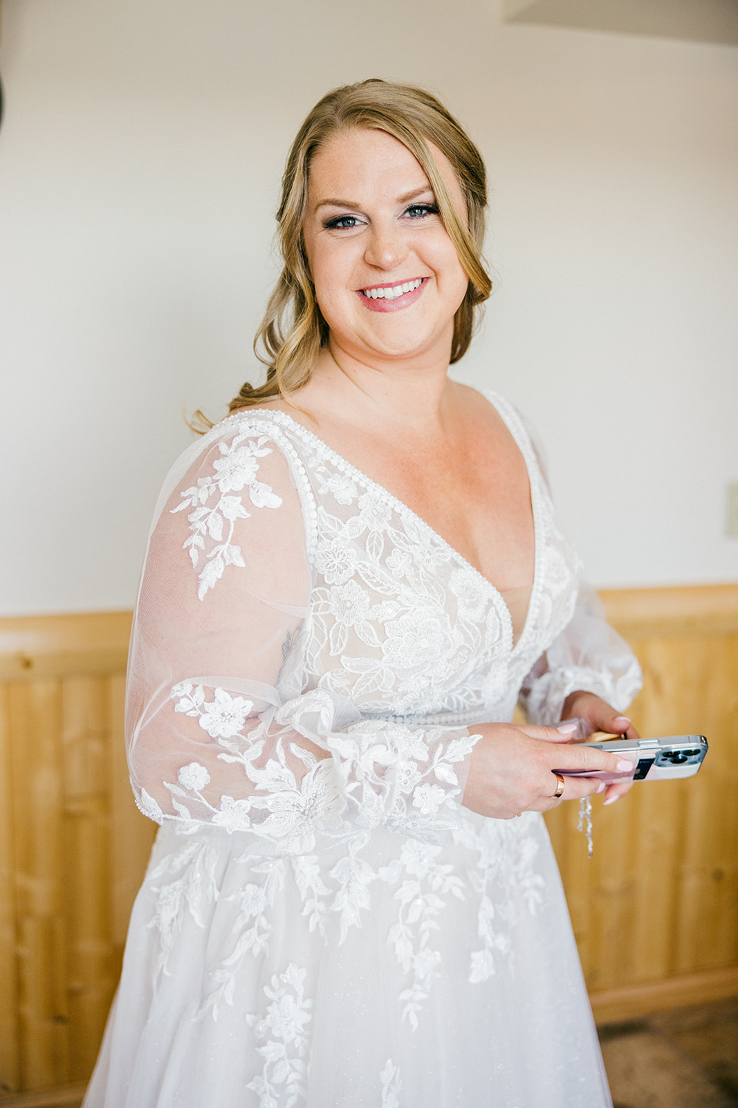 Bride in lace long-sleeve V-neck gown smiling before the ceremony, knotty pine walls of the Legacy Clubhouse getting-ready room — Tim Larsen Photography, Brainerd Lakes MN