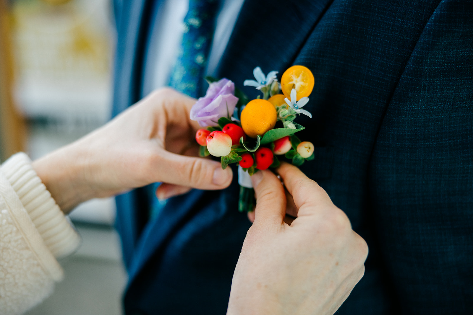 Groom's colorful boutonnière being pinned — small orange fruit, red berries, purple bloom, and greenery — Tim Larsen Photography, Brainerd Lakes MN