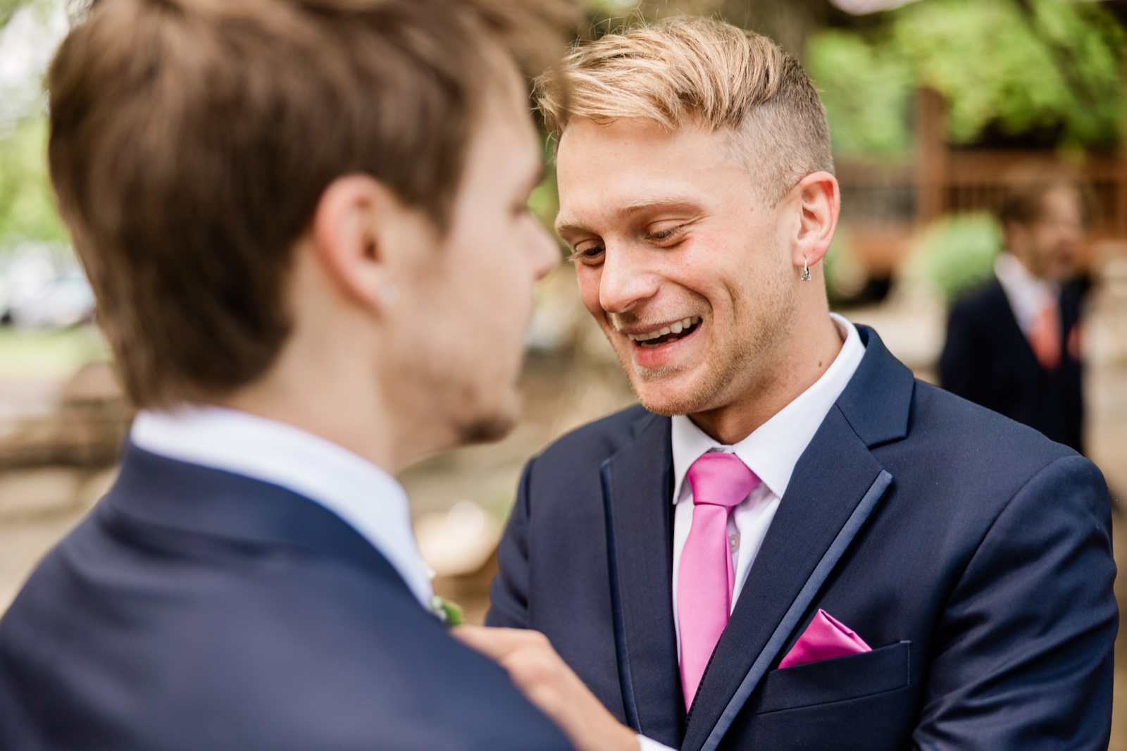 Groom laughing as a groomsman pins his boutonniere outdoors — Tim Larsen Photography, Brainerd Lakes MN