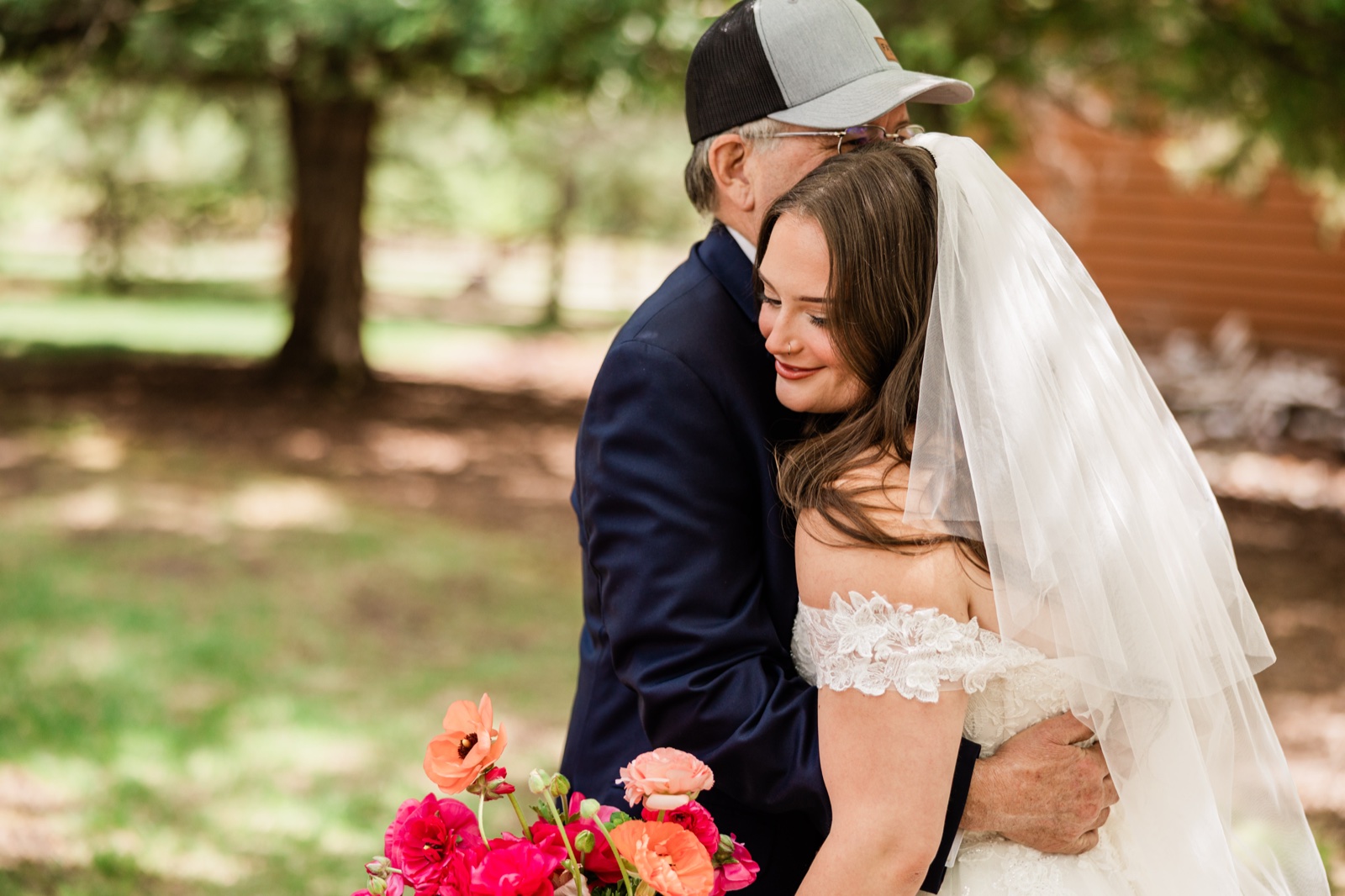 Bride and her father sharing a long hug before the ceremony, coral bouquet in the foreground