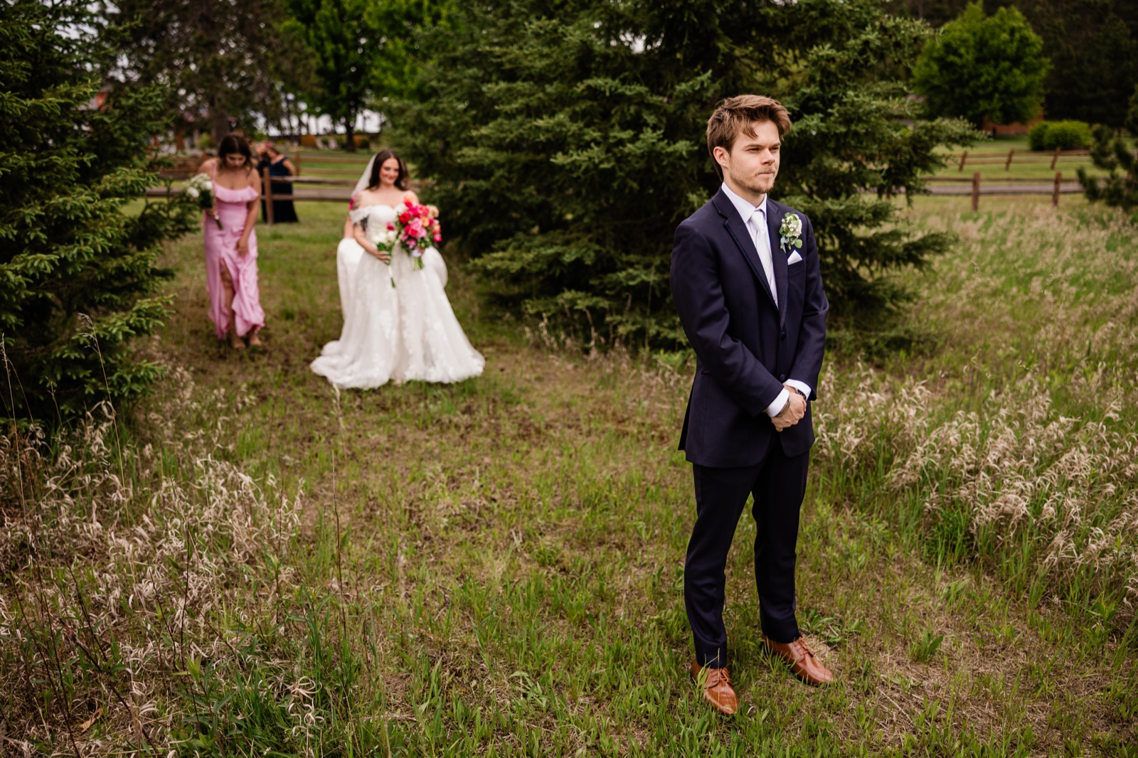 Groom waiting in a Pine Peaks meadow while the bride approaches through evergreens