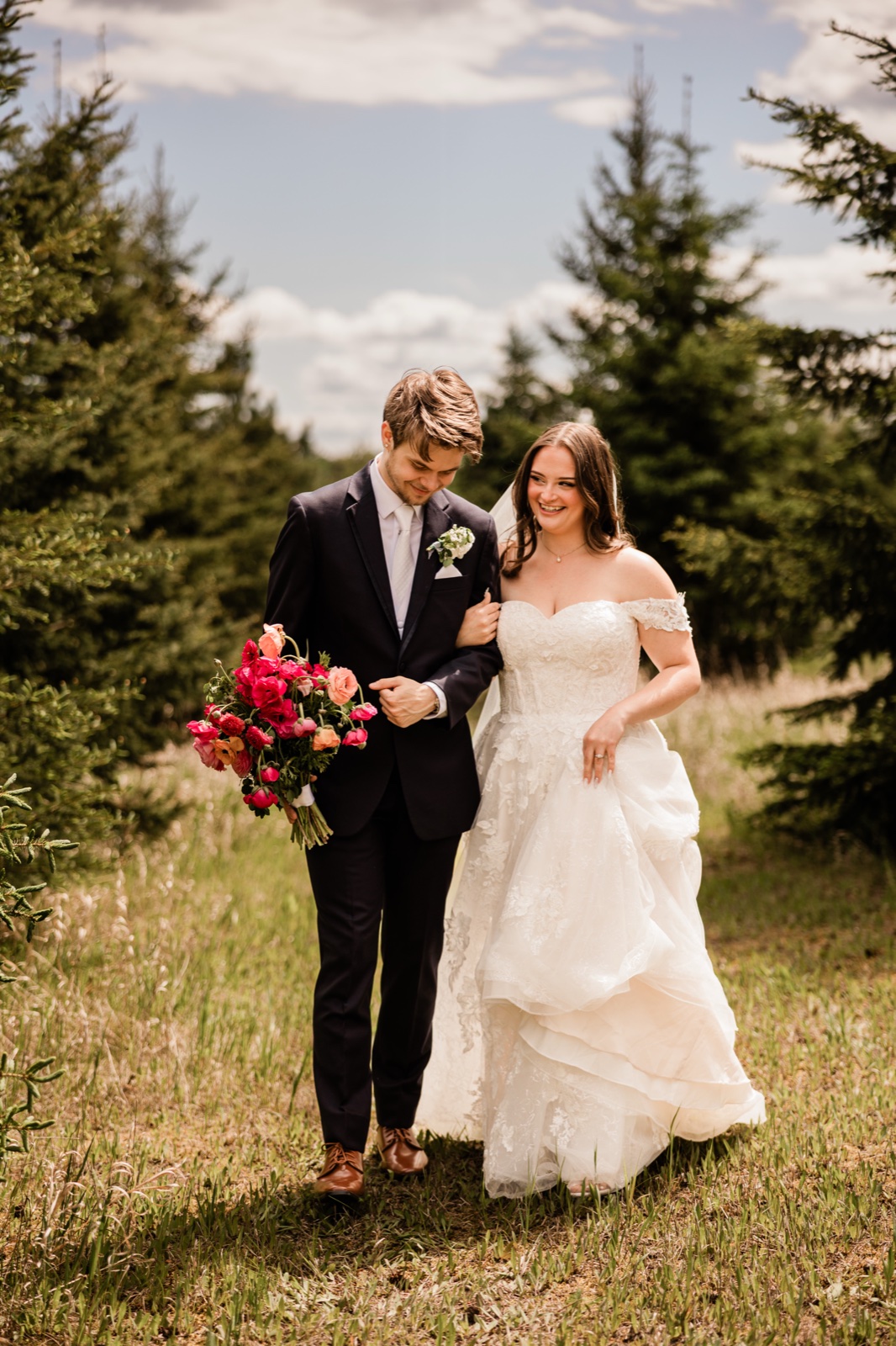 Bride and groom walking arm-in-arm through an evergreen clearing at Pine Peaks