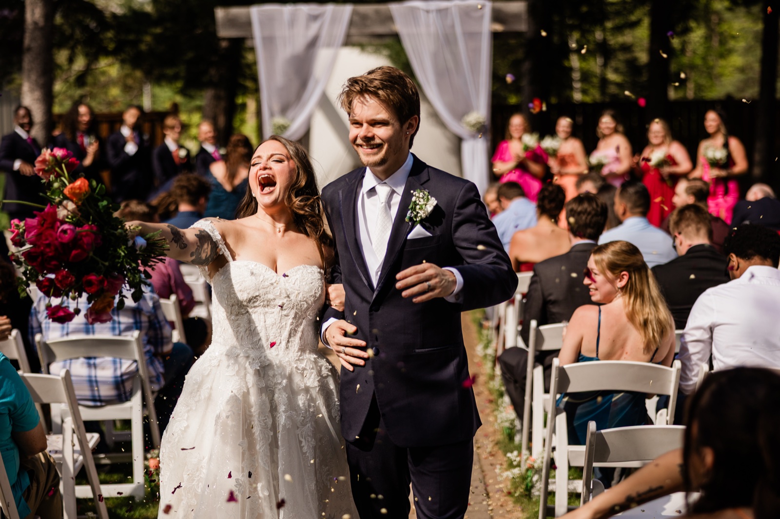 Bride laughing open-mouthed with her bouquet raised during the recessional at Pine Peaks