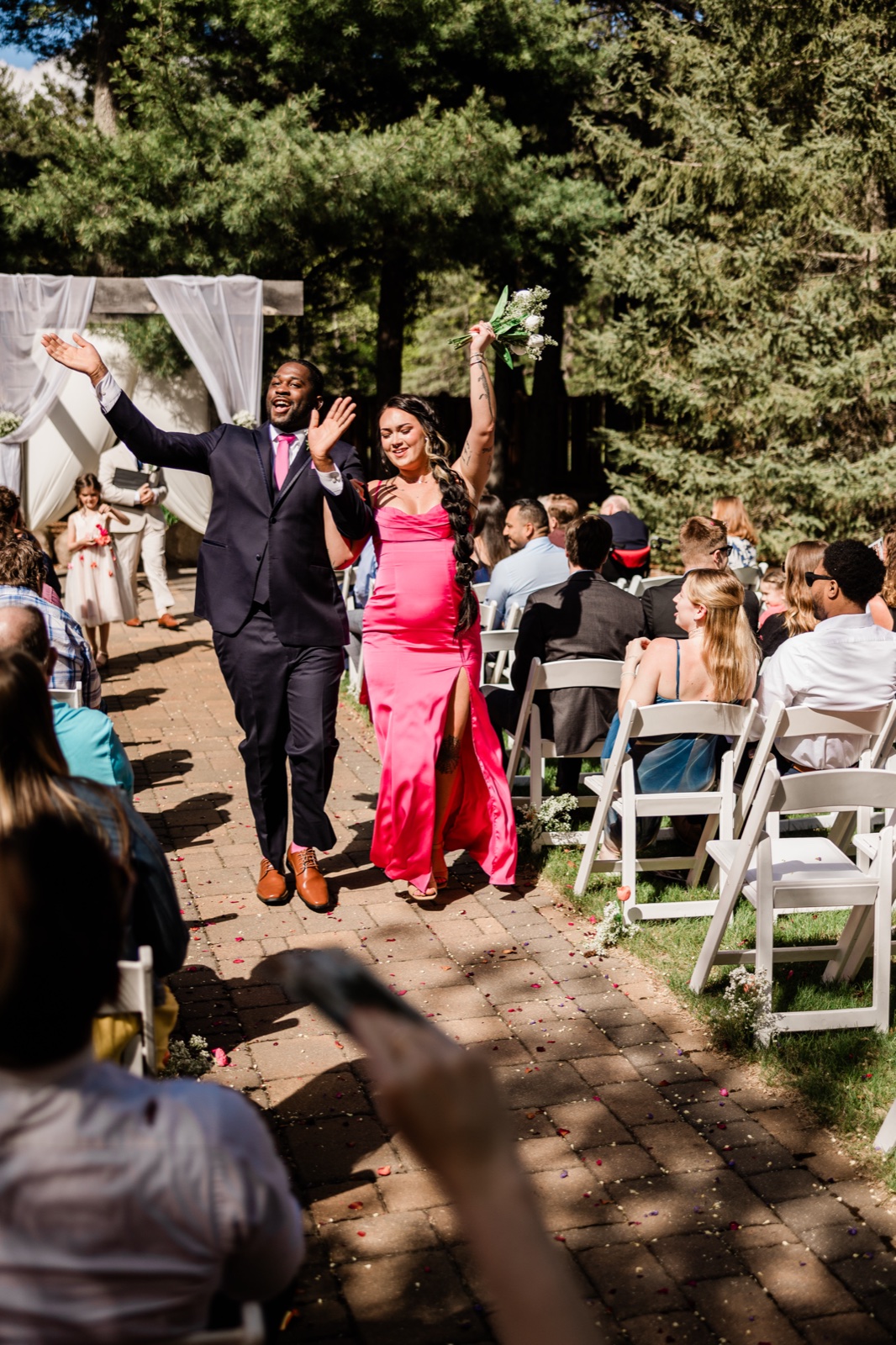 Bridesmaid and groomsman cheering with arms raised during the bridal party recessional