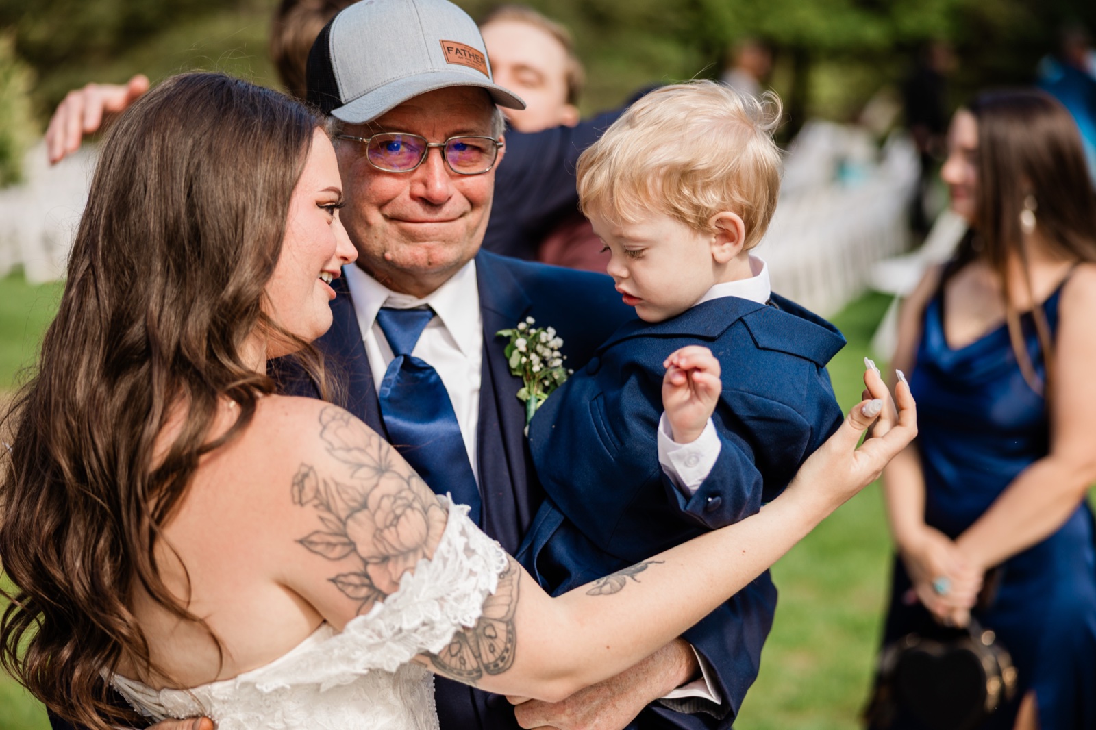 Bride with her father holding a small boy in a navy suit right after the ceremony