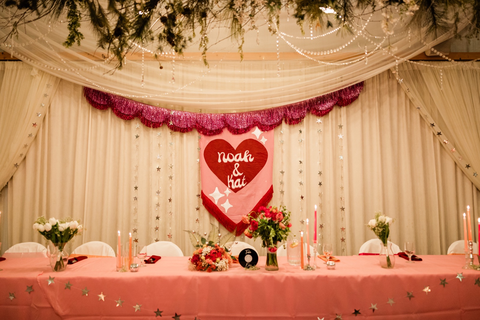 Sweetheart table with pink banner, draped fabric, star garlands and tapers at the Pine Peaks reception