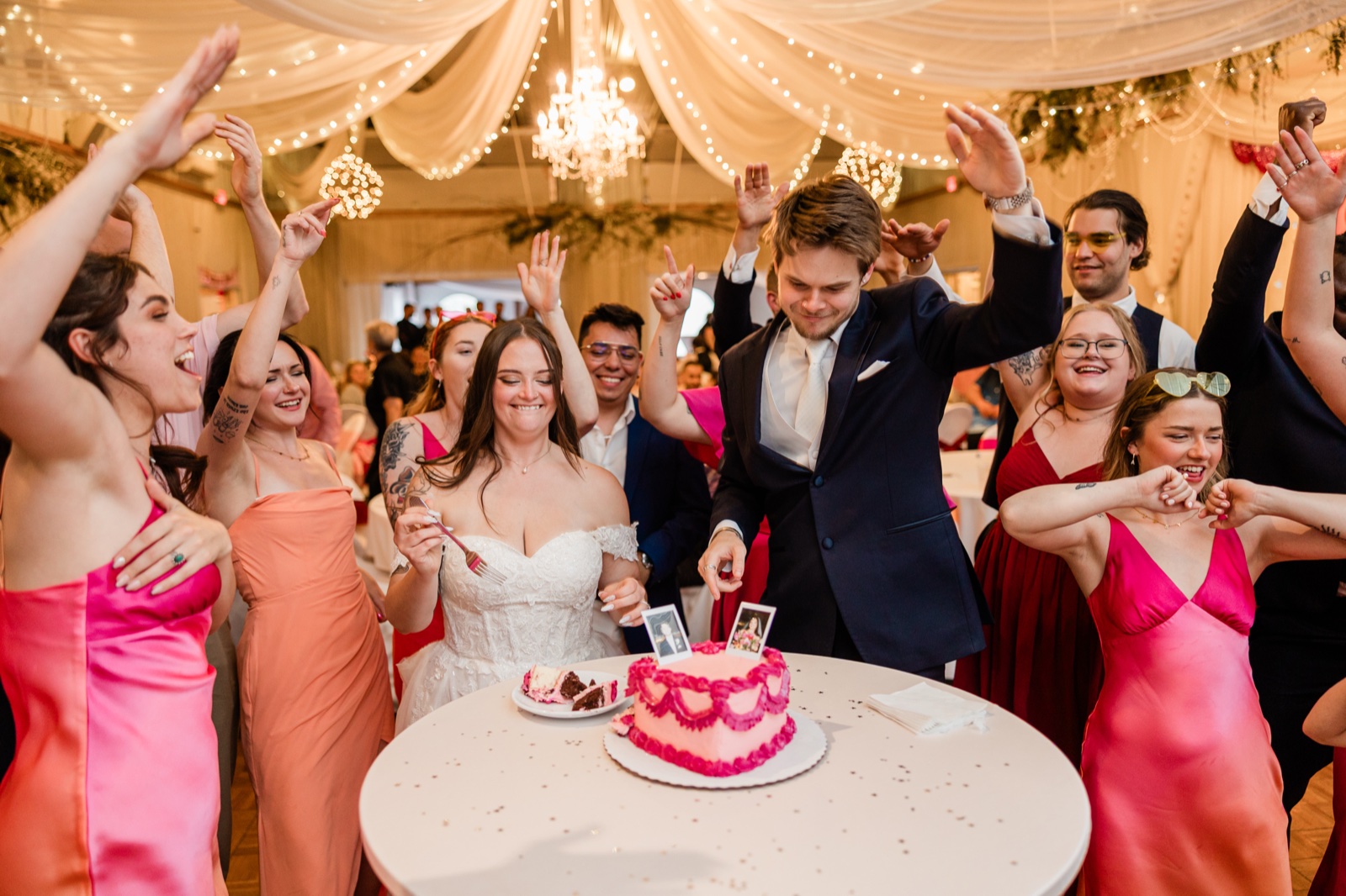 Bride and groom cutting a hot-pink heart-shaped cake as the bridal party celebrates around them