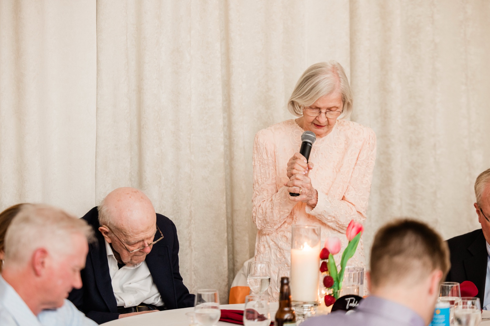 Grandmother offering a blessing with the microphone at the candlelit head table