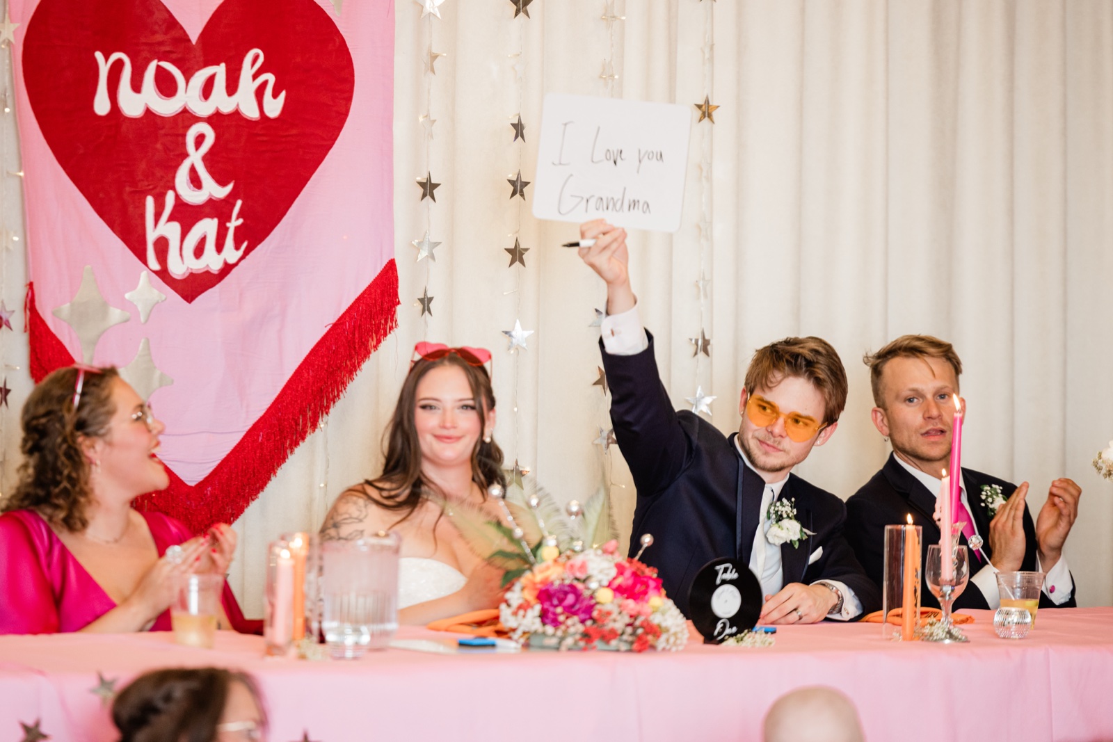 Groom raising a handwritten "I love you Grandma" sign at the head table during toasts