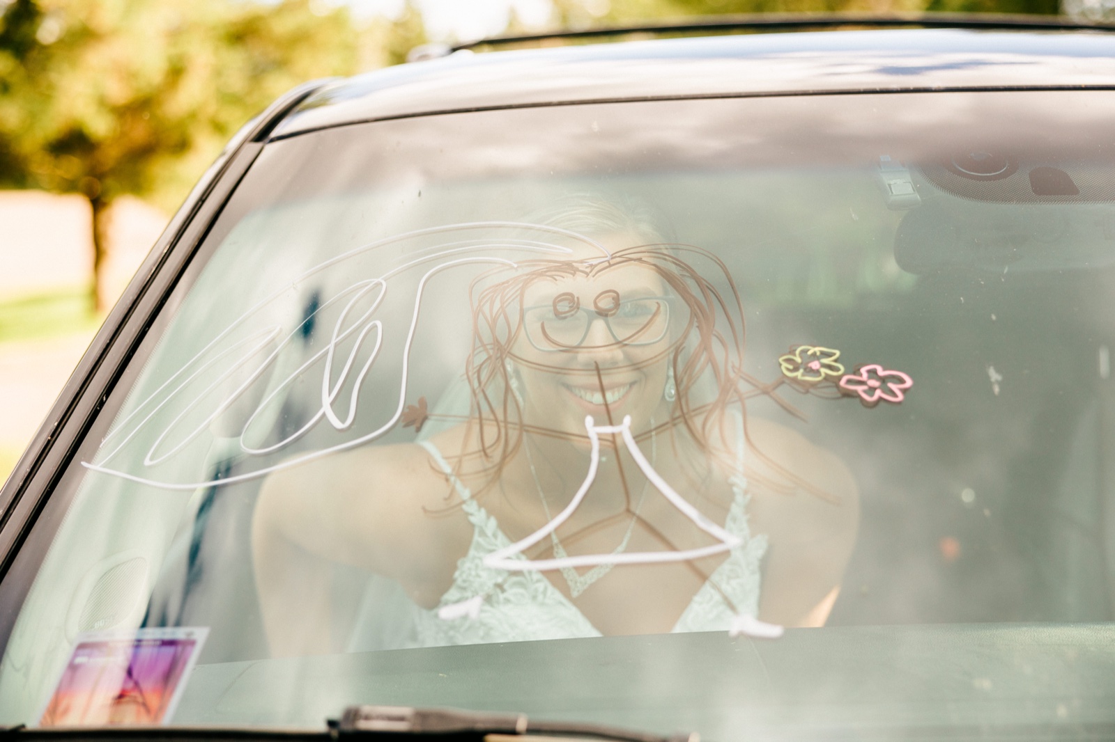 The bride smiles through a getaway-car windshield decorated with painted flowers and a 'just married' design — Tim Larsen Photography, Brainerd Lakes MN