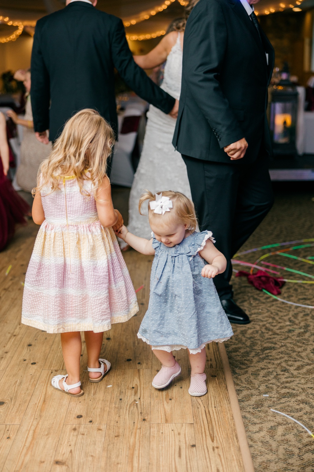 Two small girls in pastel dresses stand on the dance floor holding hands with the bride and groom — Tim Larsen Photography, Brainerd Lakes MN