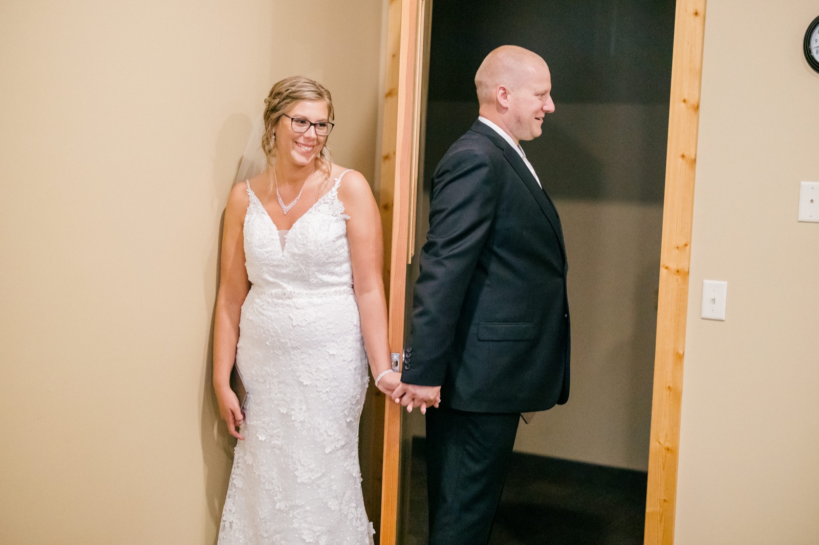 Kim smiles widely while holding hands with Jesse around a doorframe that separates them before their first look — Tim Larsen Photography, Brainerd Lakes MN