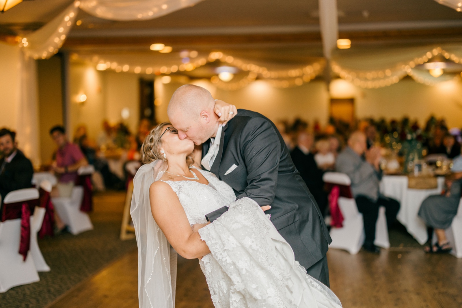 Kim and Jesse kiss on the dance floor with her veil sweeping behind them, beneath draped fabric and string lights with seated guests visible in the background — Tim Larsen Photography, Brainerd Lakes MN