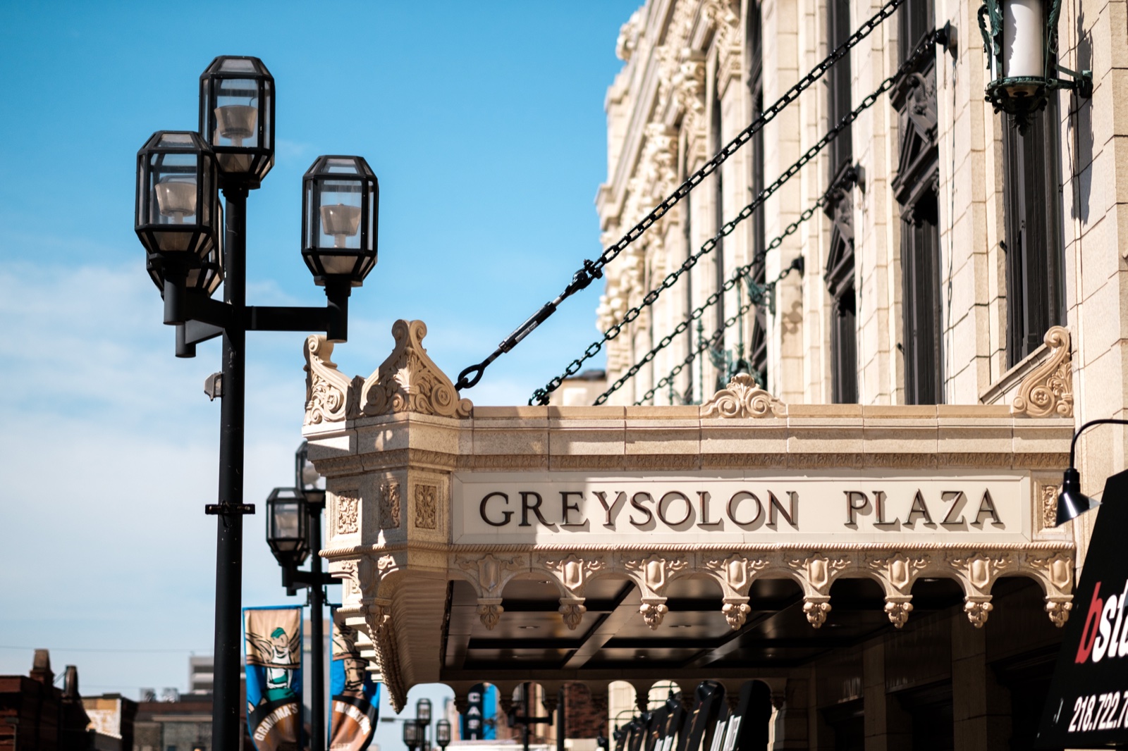 The ornate cream-colored marquee of the Greysolon Plaza in downtown Duluth, vintage lampposts and canopy chains framed against a clear blue sky — Tim Larsen Photography, Duluth MN