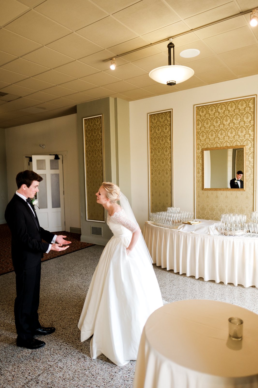 The bride laughs as the groom reacts to seeing her, his reflection visible in a gilded mirror across the Greysolon Ballroom — Tim Larsen Photography, Duluth MN