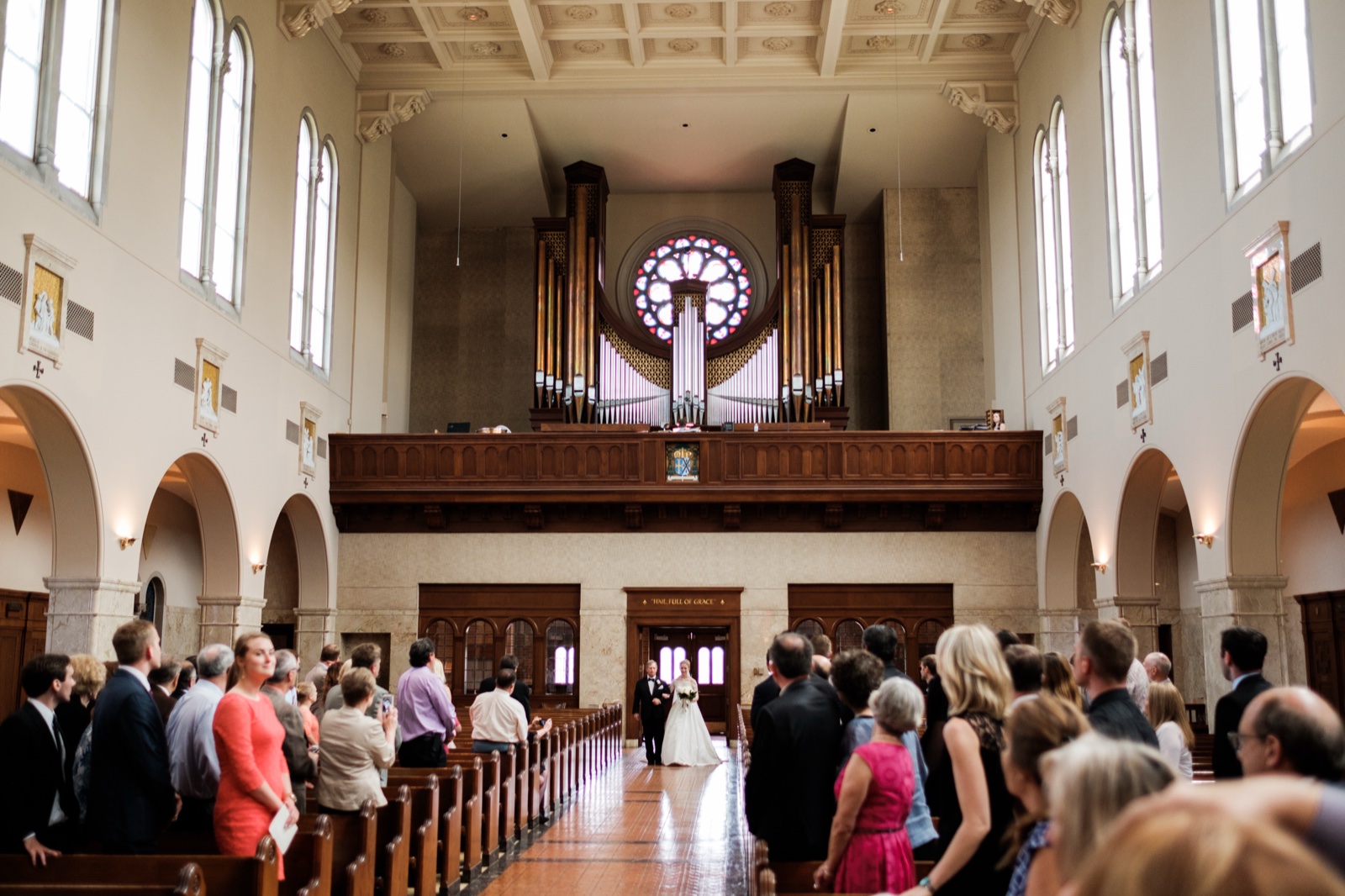 The bride and her father at the far end of the long Cathedral aisle beneath the massive pipe organ and stained-glass rose window as guests rise from the pews on either side — Tim Larsen Photography, Duluth MN