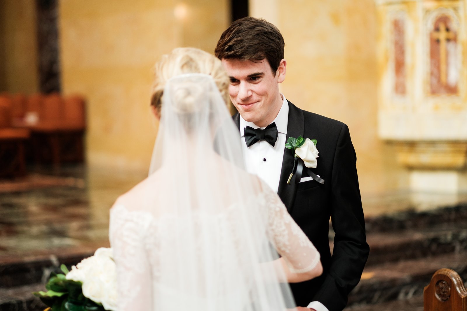 The groom smiles softly at his veiled bride during the ceremony inside the warm marble Cathedral of Our Lady of the Rosary — Tim Larsen Photography, Duluth MN