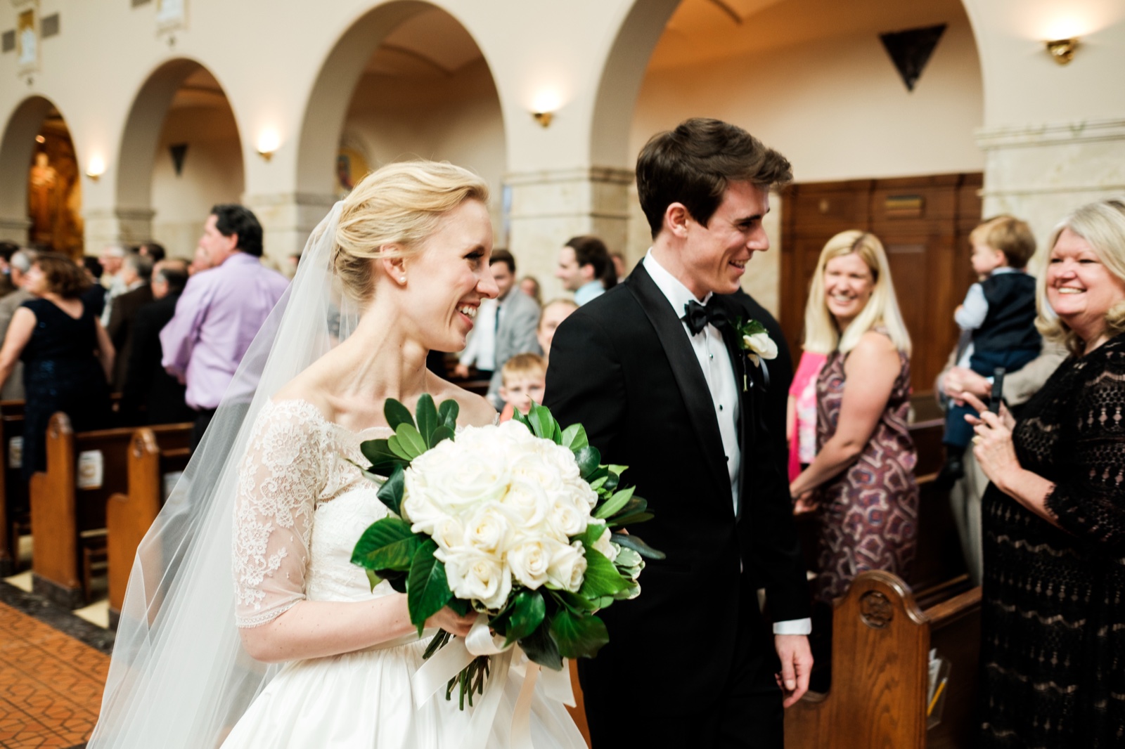 The bride and groom laugh widely walking back down the aisle just after their ceremony, guests applauding from the pews on either side — Tim Larsen Photography, Duluth MN