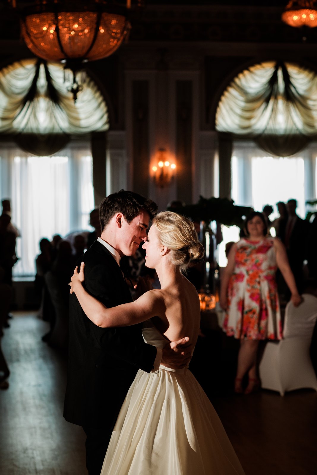 The bride and groom share a forehead-to-forehead first dance in the ornate Greysolon Ballroom, framed tightly under glowing chandeliers and curtained alcoves — Tim Larsen Photography, Duluth MN