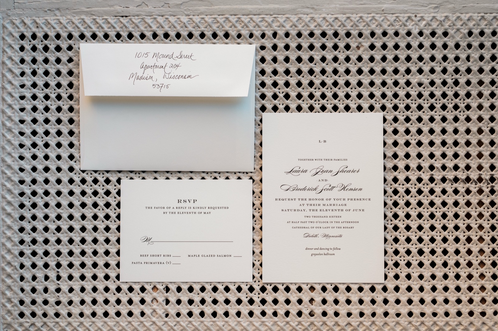 The Larsen letterpress wedding invitation suite — handwritten envelope, RSVP card, and main invite arranged on a textured woven cane background — Tim Larsen Photography, Duluth MN