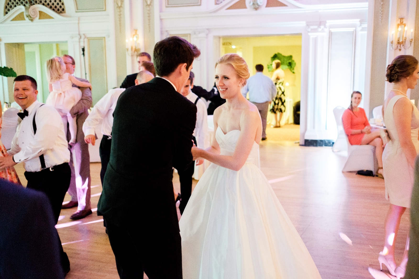 The bride smiles over her shoulder mid-spin on the open dance floor with the groom in the ornate Greysolon Ballroom while guests laugh and watch from the edges — Tim Larsen Photography, Duluth MN