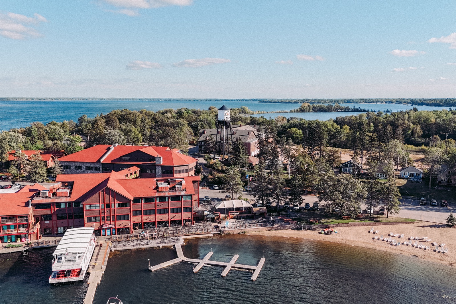 An aerial view of Breezy Point Resort showing red-roofed lodge buildings, the historic water tower, a docked paddleboat, and the sandy shoreline of Pelican Lake — Tim Larsen Photography, Brainerd Lakes MN