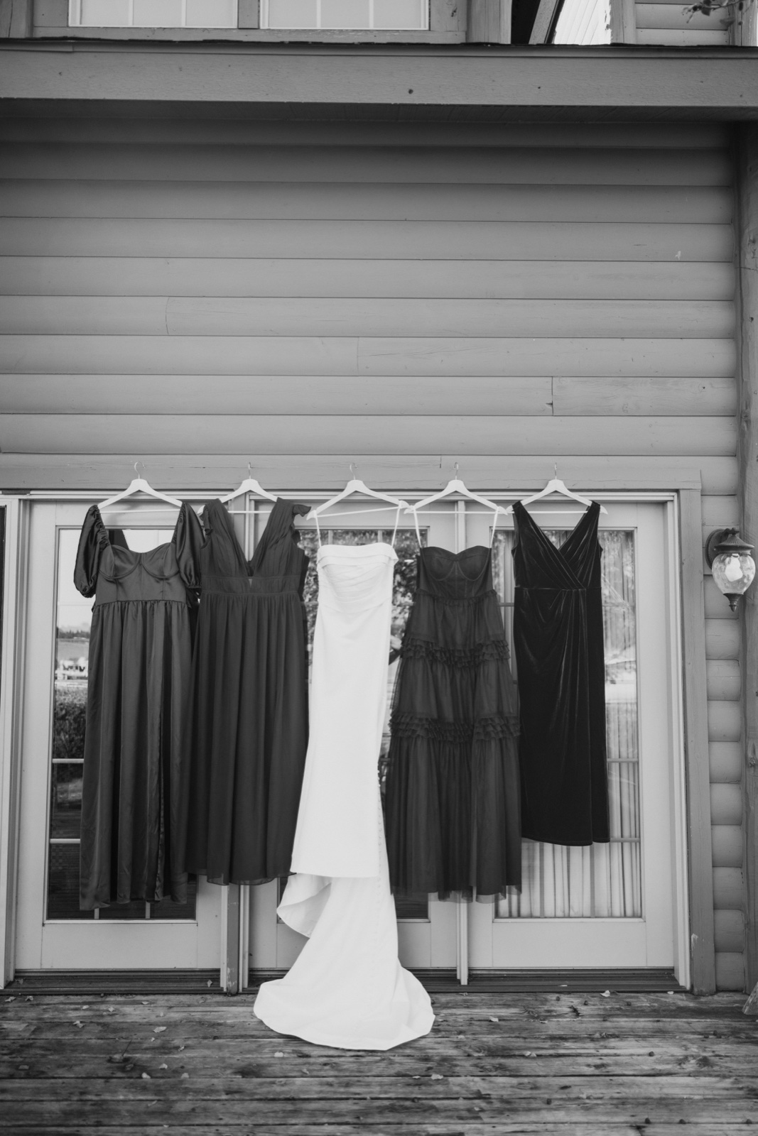 The bride's white gown hangs centered between five bridesmaid dresses on hangers along the exterior of a cabin porch — Tim Larsen Photography, Brainerd Lakes MN