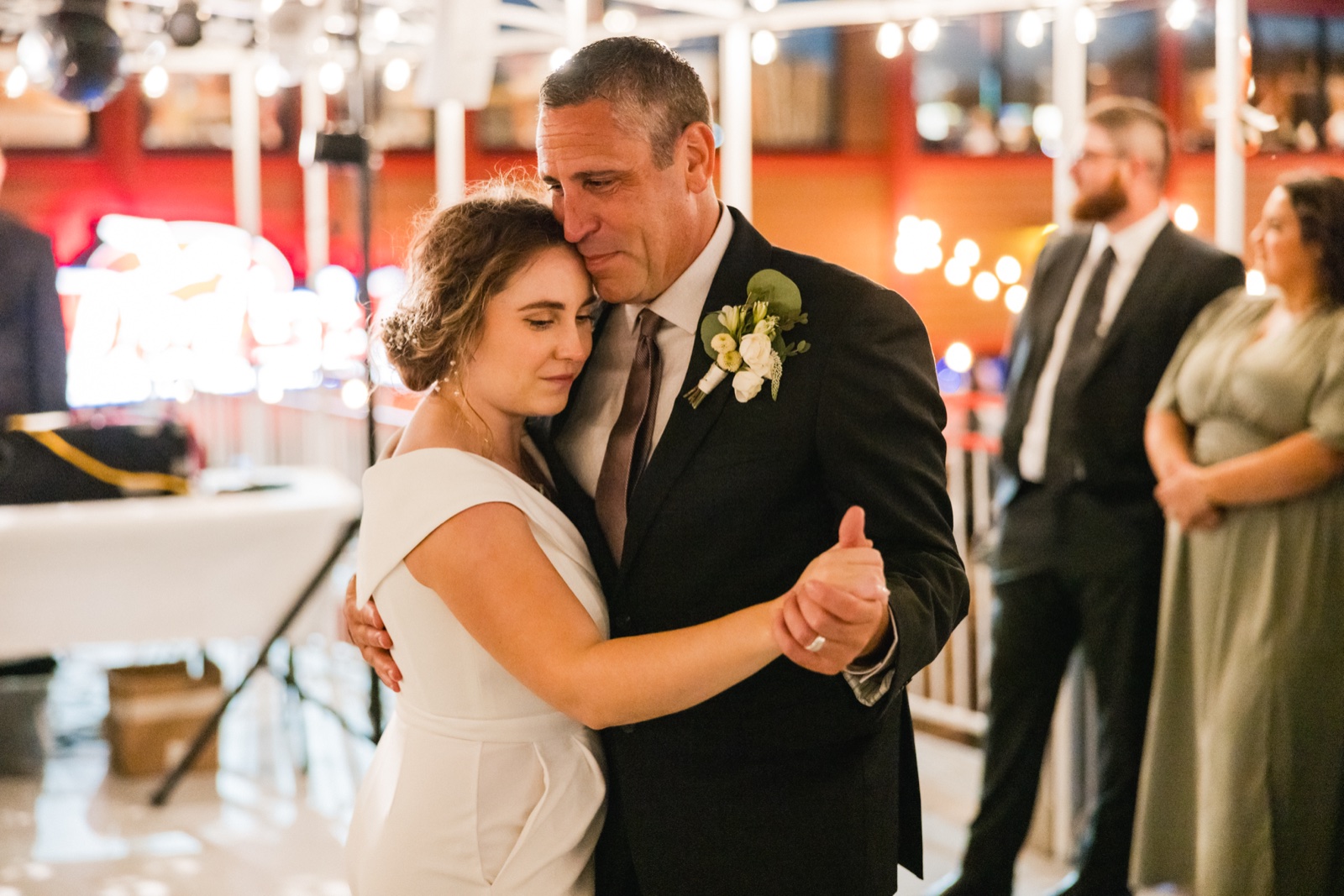 The bride leans her head against her father's shoulder during their dance, eyes closed, with warm string lights glowing in the background — Tim Larsen Photography, Brainerd Lakes MN