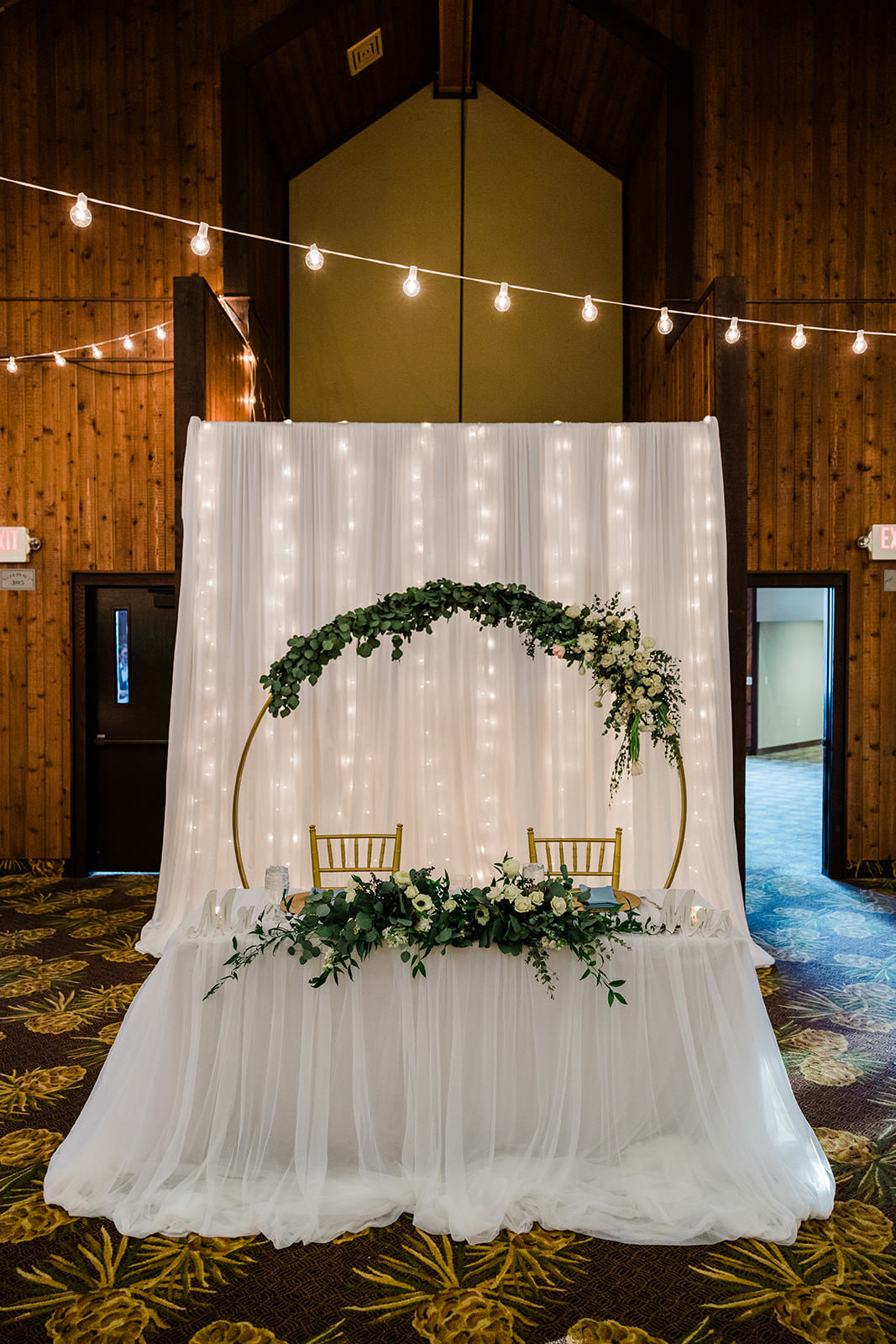 Sweetheart table with gold hoop, greenery, and fairy light backdrop — Grand View Lodge reception — Tim Larsen Photography, Brainerd Lakes MN