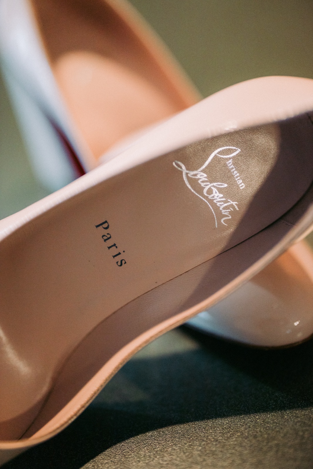A close-up of nude Christian Louboutin Paris bridal heels resting on their sides, the signature script logo visible on the inner sole — Tim Larsen Photography, Brainerd Lakes MN