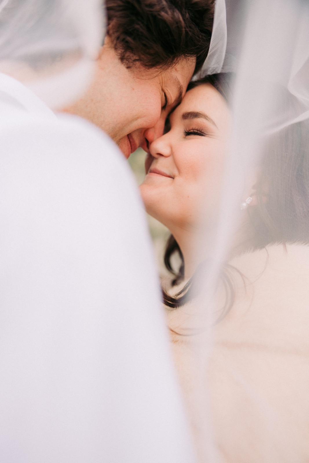 The bride smiles with closed eyes as she presses her face against the groom's, both framed by her veil draped around them — Tim Larsen Photography, Brainerd Lakes MN