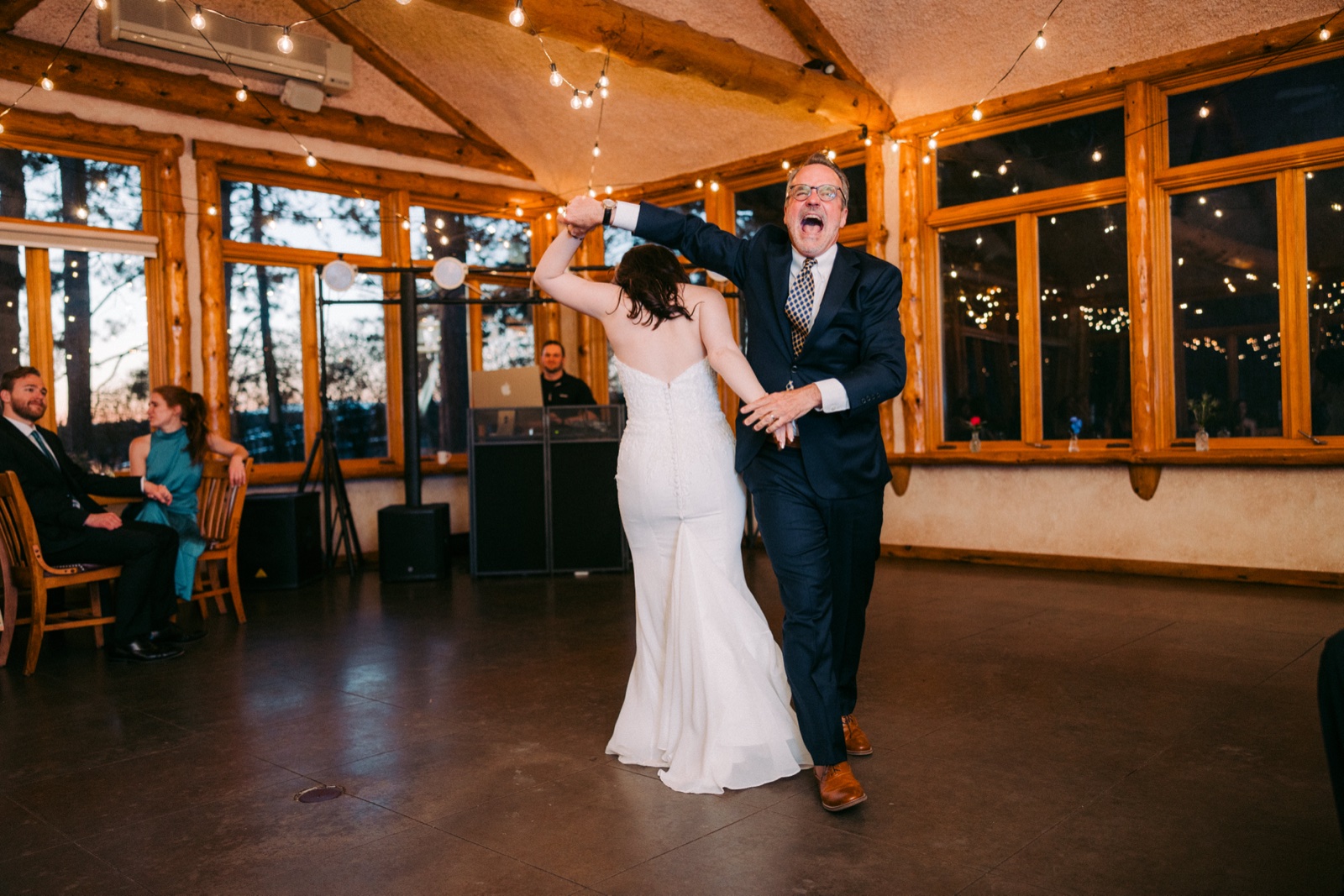 The bride twirls with her father on the dance floor as he laughs openly under string lights inside the log-beamed lodge — Tim Larsen Photography, Brainerd Lakes MN