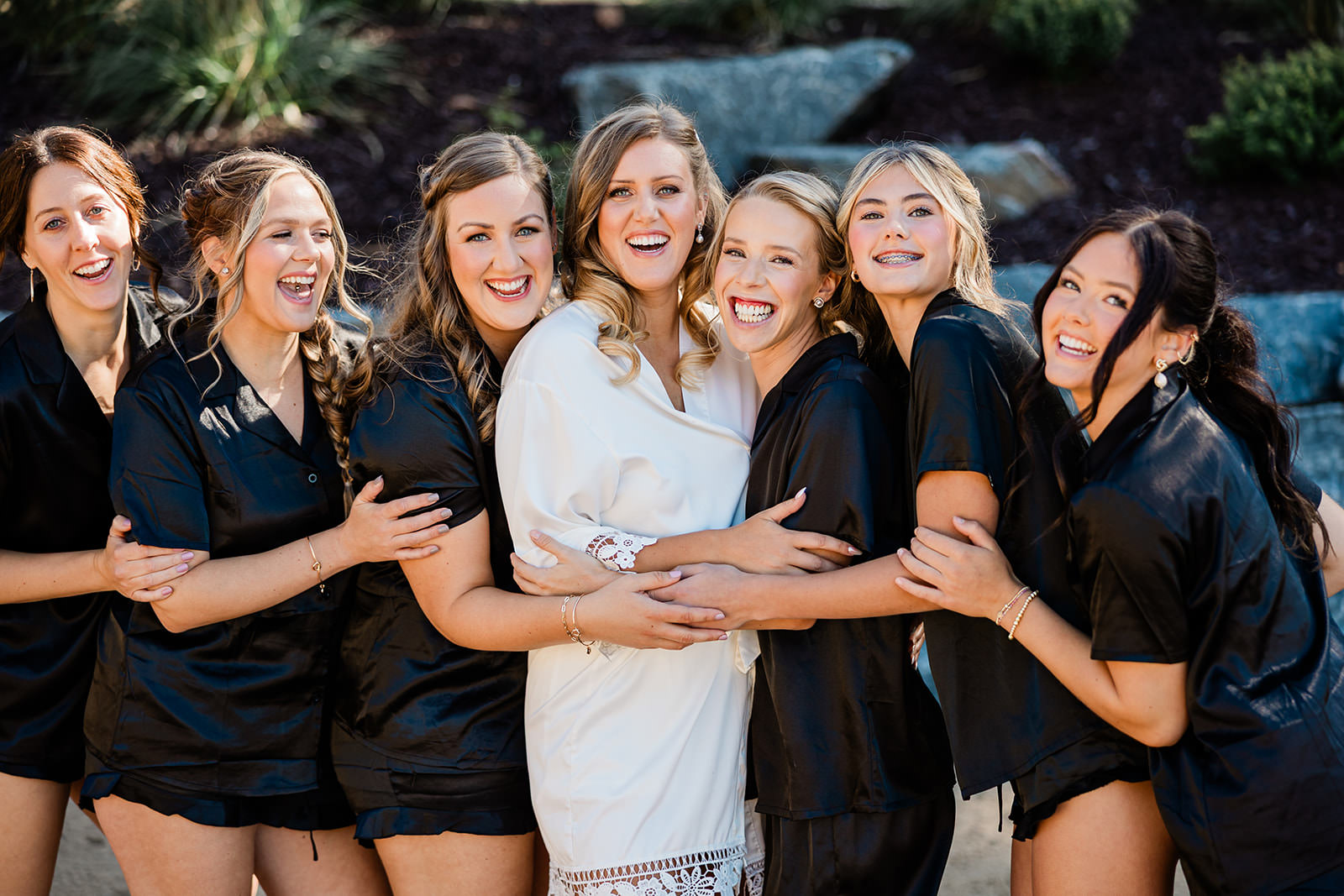 Bride and bridesmaids in black robes laughing together outside The Cove on Whitefish Lake