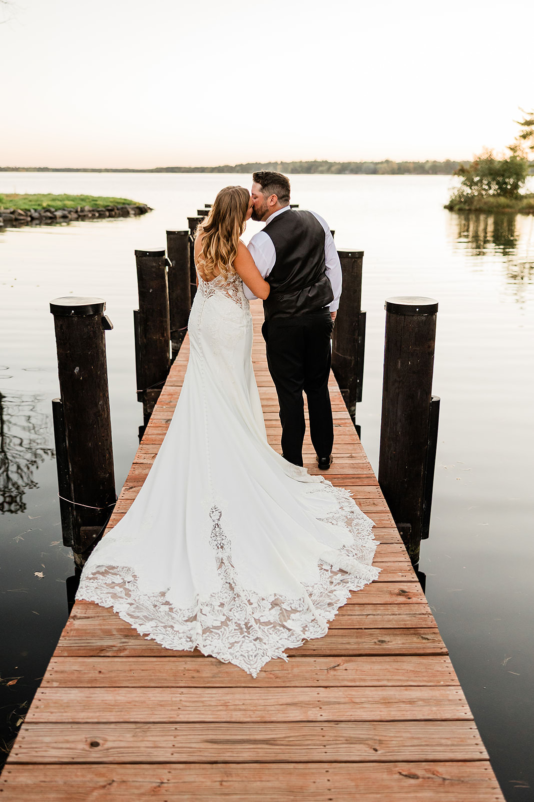 Bride and groom from behind on the dock at sunset — lace train on the dock, Whitefish Lake