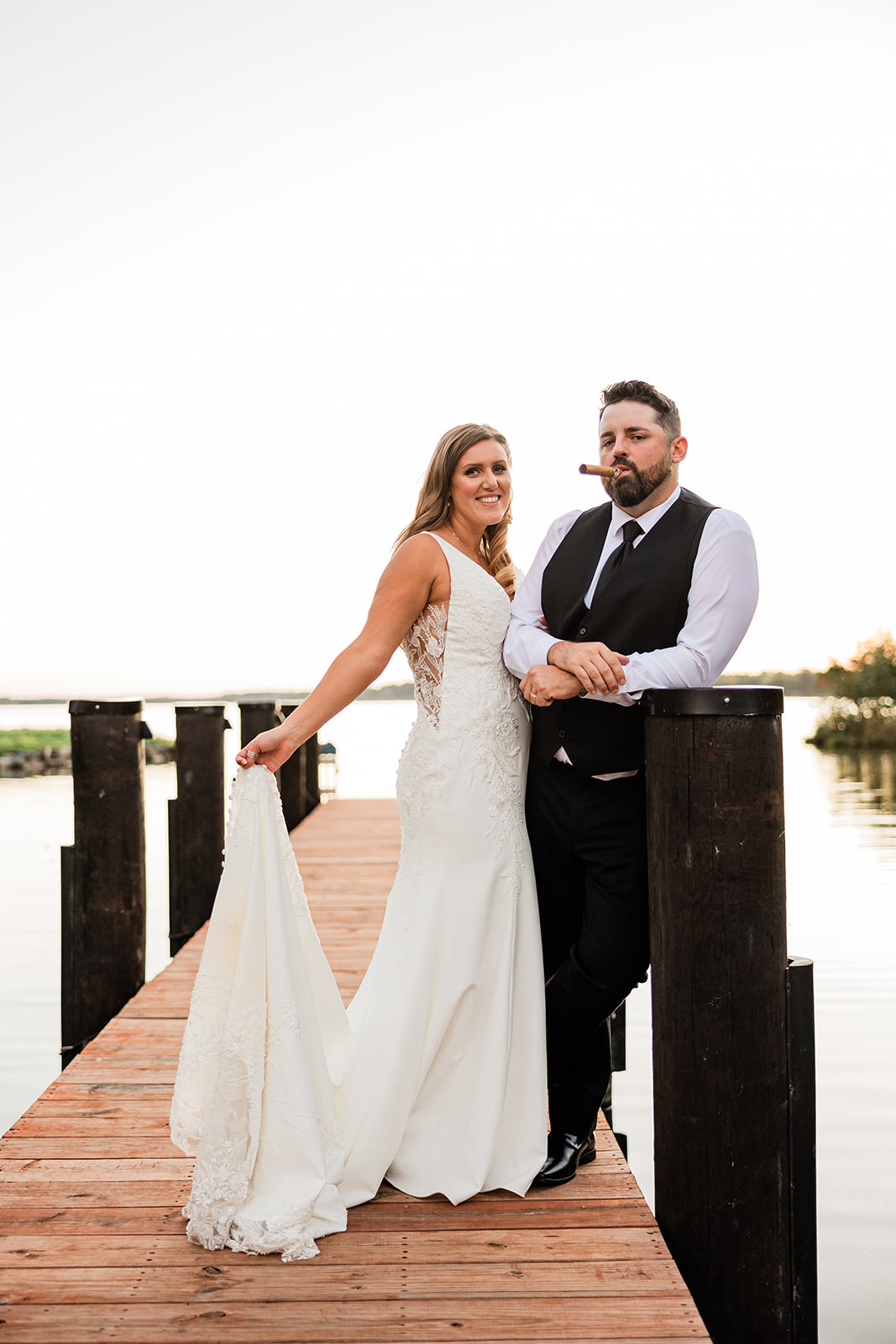 Editorial portrait of bride and groom on the dock — groom with cigar, bride holding train, Whitefish Lake