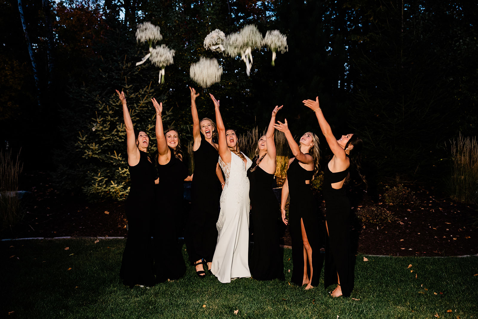Bouquet toss with bridesmaids in black dresses — nighttime reception at The Cove