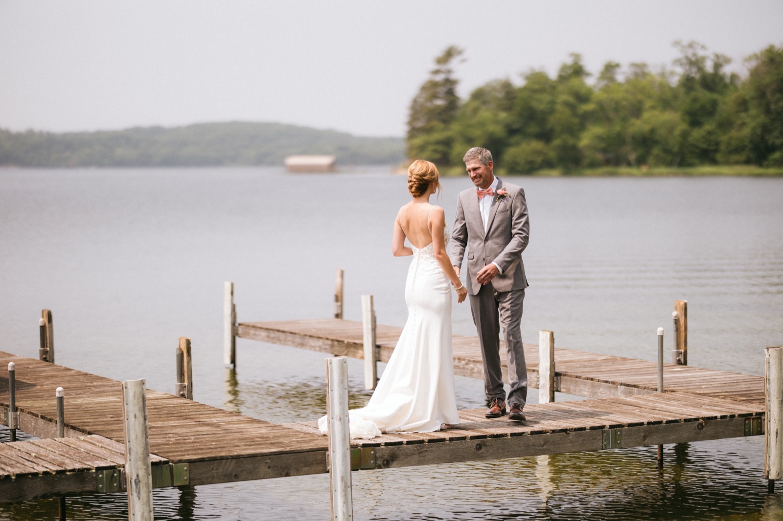 Melissa and Kody hold hands at the end of a wooden dock extending into Gull Lake under an overcast summer sky — Tim Larsen Photography, Brainerd Lakes MN