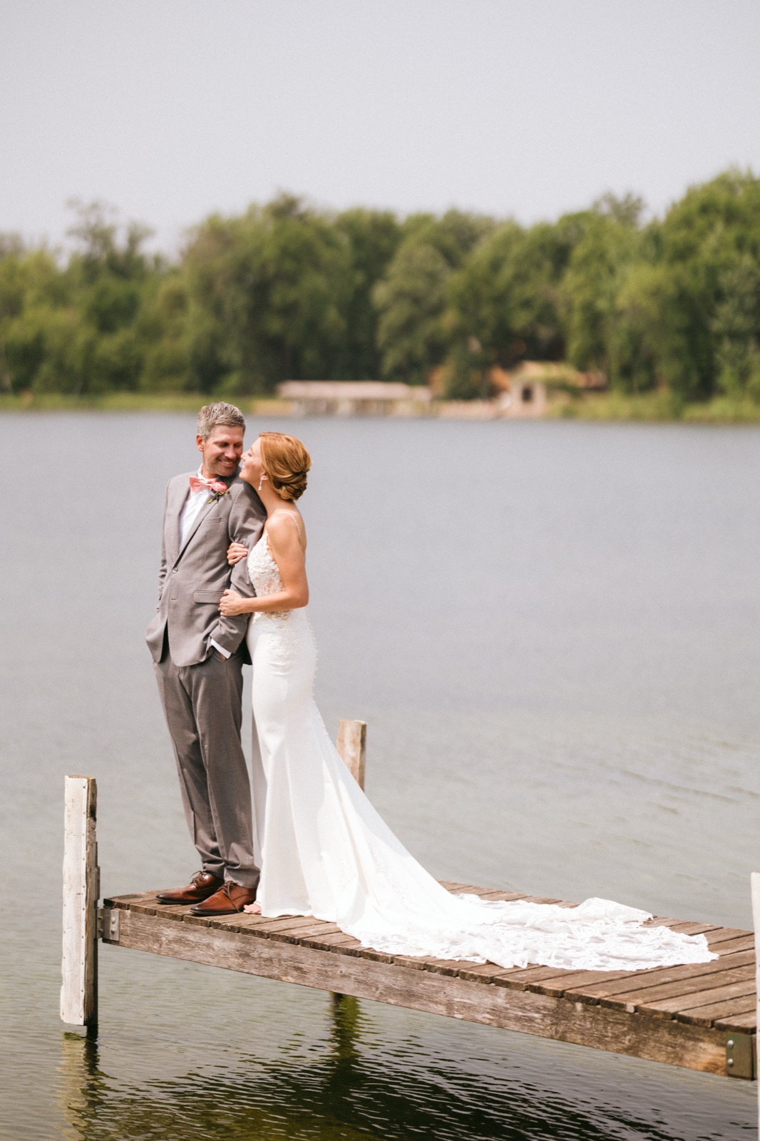 Melissa leans into Kody on a weathered wooden dock at Madden's, her long lace train spilling across the planks behind her — Tim Larsen Photography, Brainerd Lakes MN