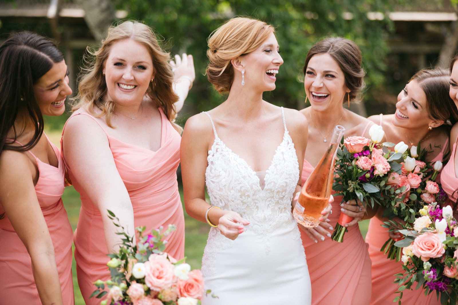 Melissa and bridesmaids in coral dresses share a laugh on the lawn at Madden's, bouquets and a bottle of rosé in hand — Tim Larsen Photography, Brainerd Lakes MN