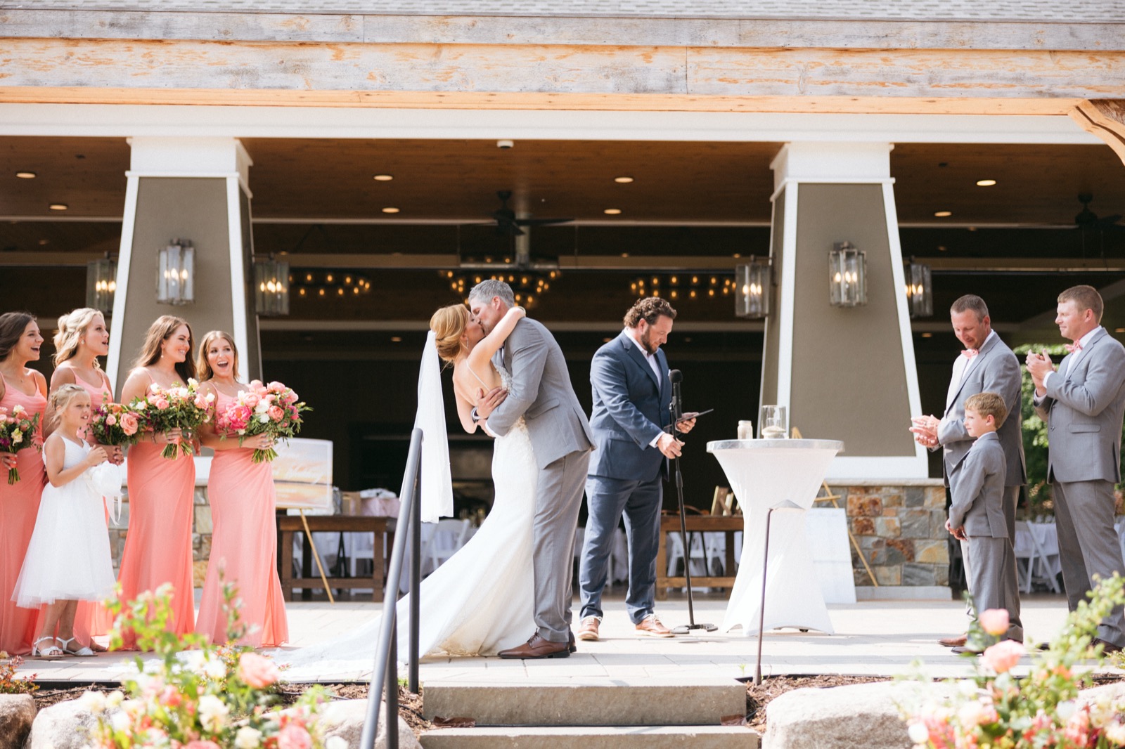 Melissa and Kody share their first kiss under the symmetrical timber columns of the Madden's pavilion as the bridal party reacts on either side — Tim Larsen Photography, Brainerd Lakes MN