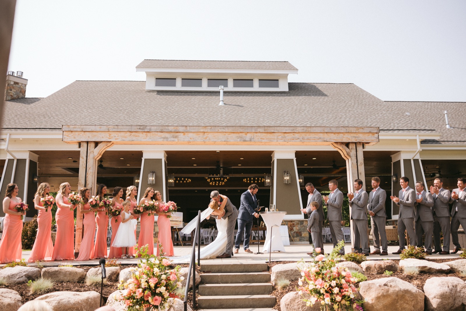 Wide symmetrical view of the recessional dip-kiss at the Madden's pavilion, bridal party flanking on both sides under the open timber ceiling — Tim Larsen Photography, Brainerd Lakes MN
