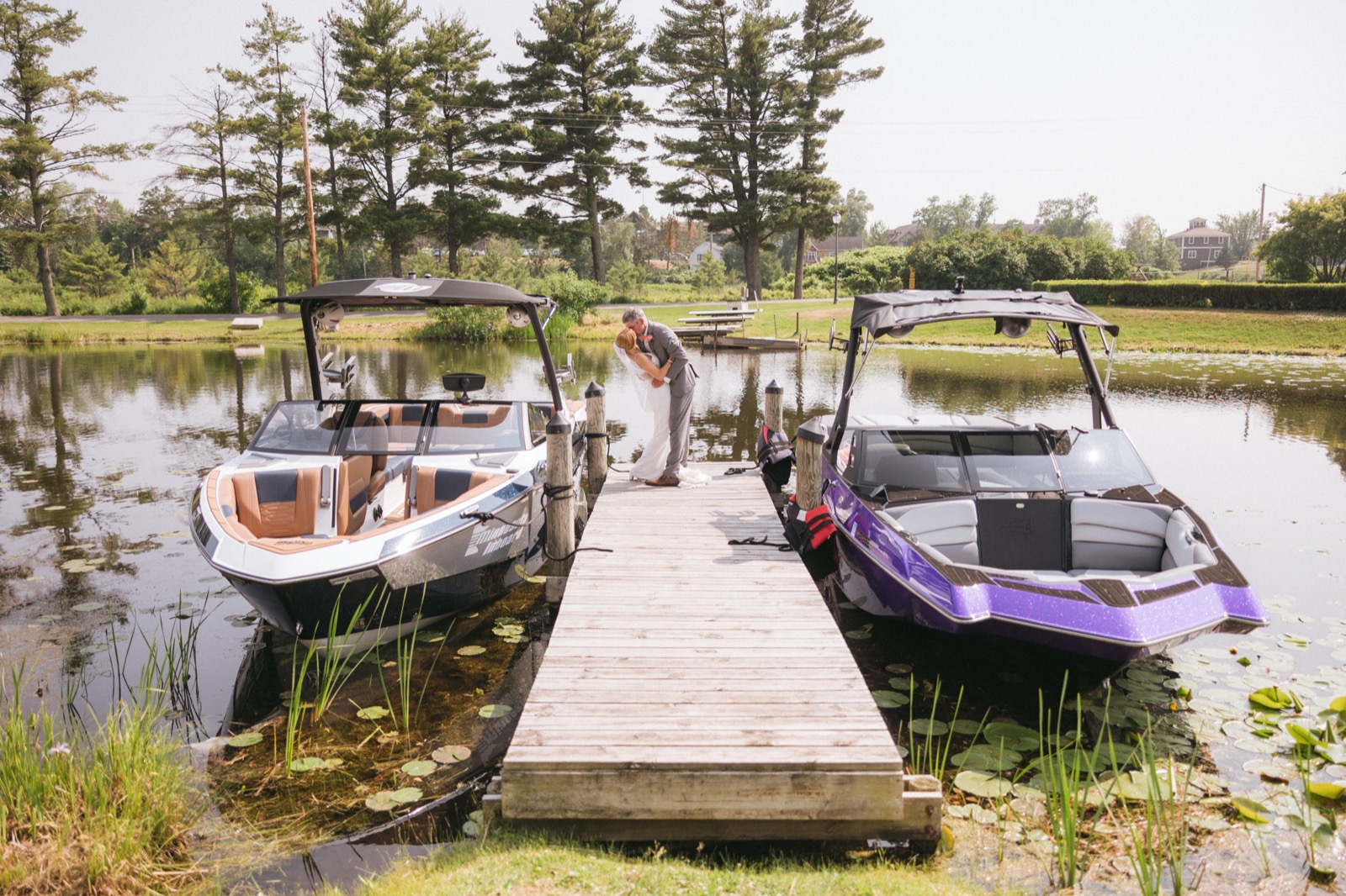Melissa and Kody share a quiet kiss at the end of a Madden's dock framed symmetrically by two boats moored on calm Gull Lake water — Tim Larsen Photography, Brainerd Lakes MN