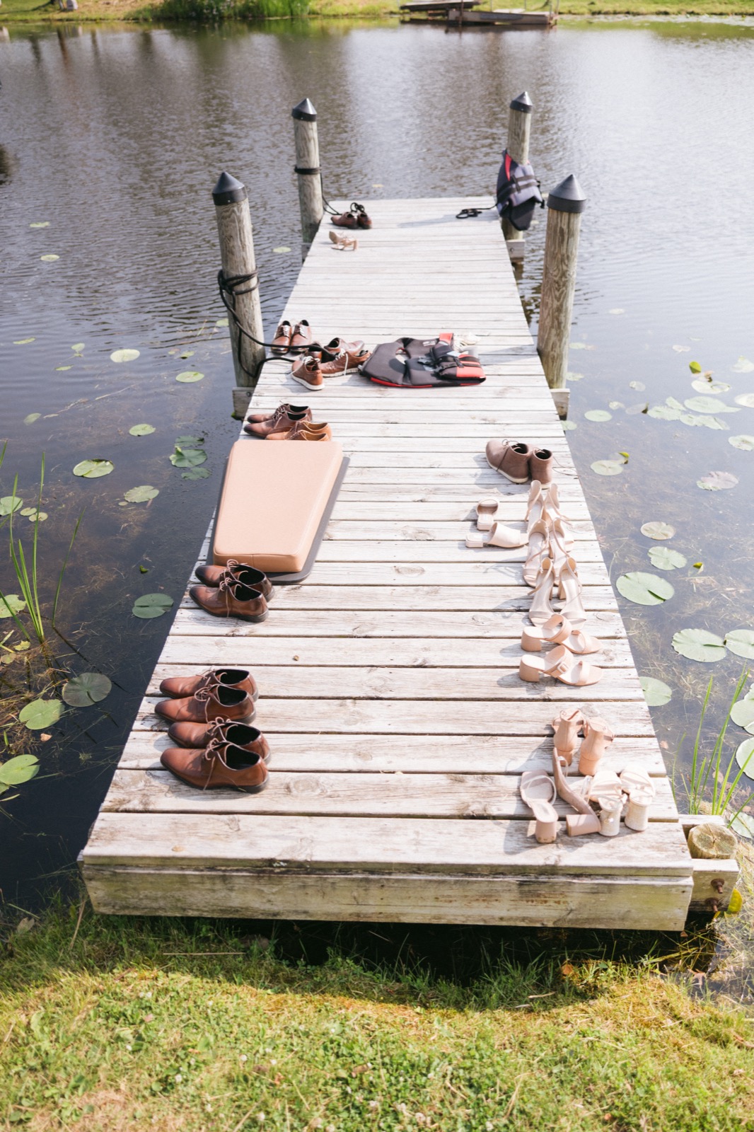 Wedding party shoes lined up along a sunny Madden's dock with a lone life vest, lily pads framing the wood — Tim Larsen Photography, Brainerd Lakes MN