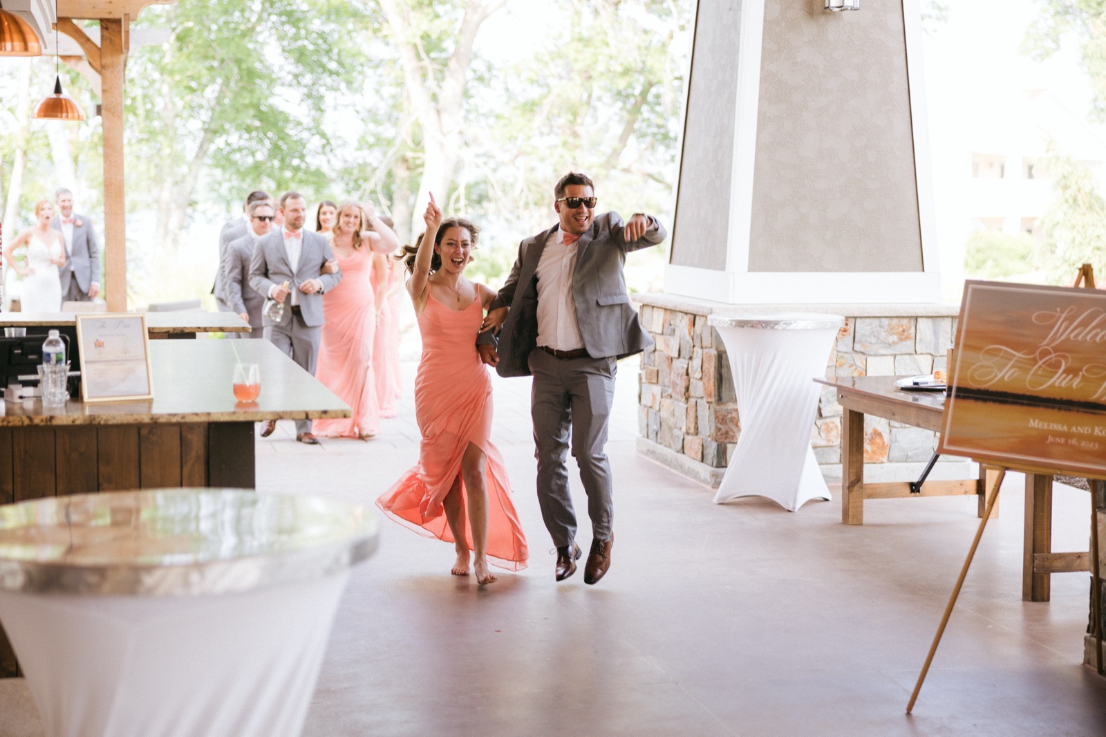 A bridesmaid in coral and a groomsman in sunglasses dance into the reception at Madden's open-air pavilion, the rest of the bridal party trailing behind — Tim Larsen Photography, Brainerd Lakes MN