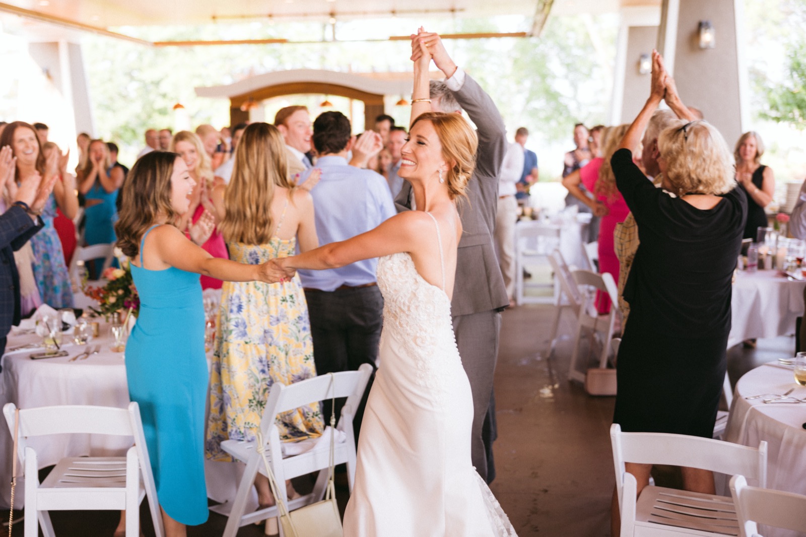 Melissa mid-twirl during the grand entrance at the Madden's reception pavilion, guests cheering with raised hands flanking the aisle — Tim Larsen Photography, Brainerd Lakes MN