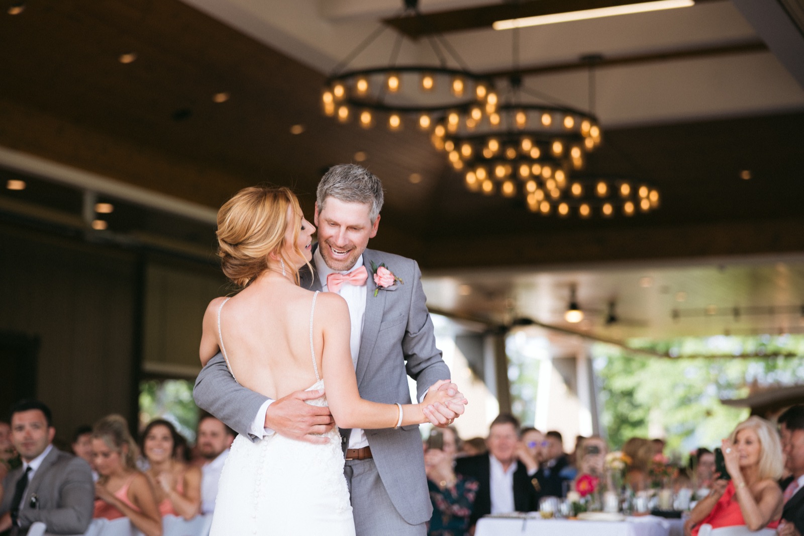 Melissa and Kody centered under chandeliers on the Madden's reception pavilion dance floor for their first dance, guests watching from the periphery — Tim Larsen Photography, Brainerd Lakes MN