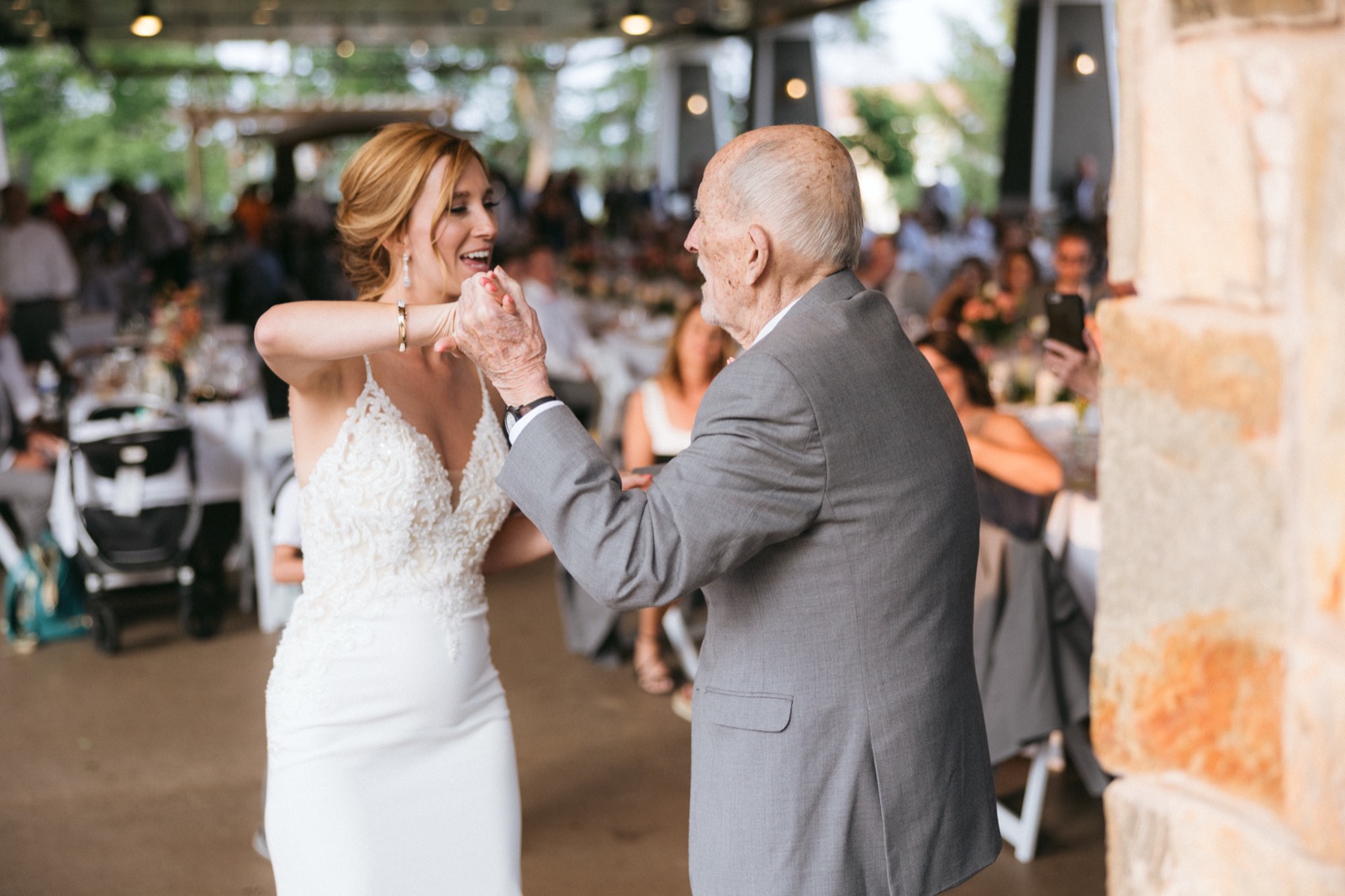 Melissa laughs joyfully while dancing with her father in a gray suit, framed by a stone pillar in the Madden's reception pavilion — Tim Larsen Photography, Brainerd Lakes MN