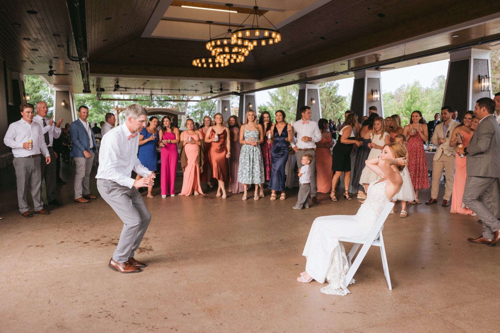 Melissa covers her ears in a chair while Kody crouches across the dance floor preparing for the garter toss at the chandelier-lit Madden's pavilion — Tim Larsen Photography, Brainerd Lakes MN