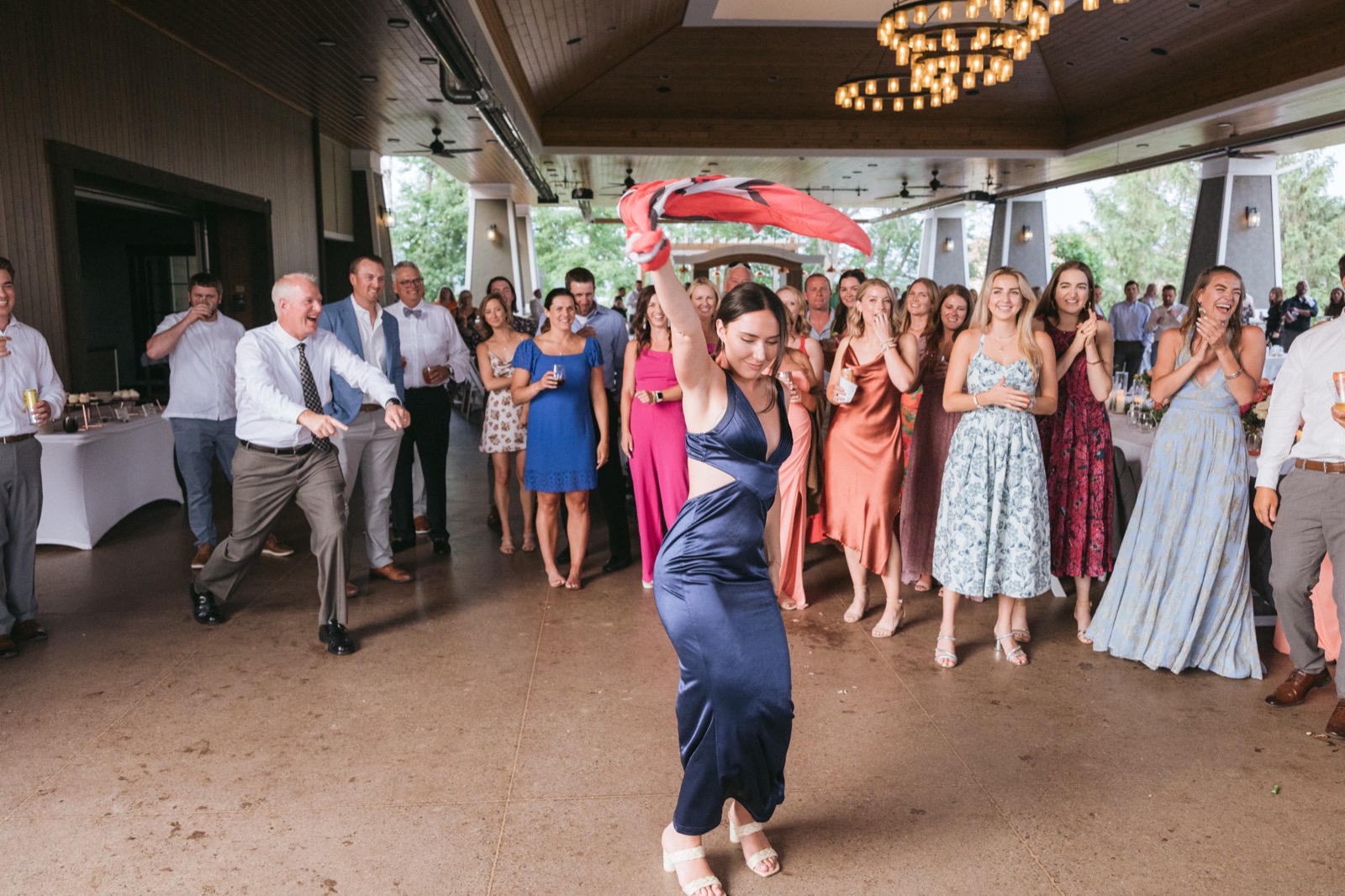 A guest mid-twirl on the Madden's pavilion dance floor with a flag overhead, ringed by cheering guests under the chandeliers — Tim Larsen Photography, Brainerd Lakes MN