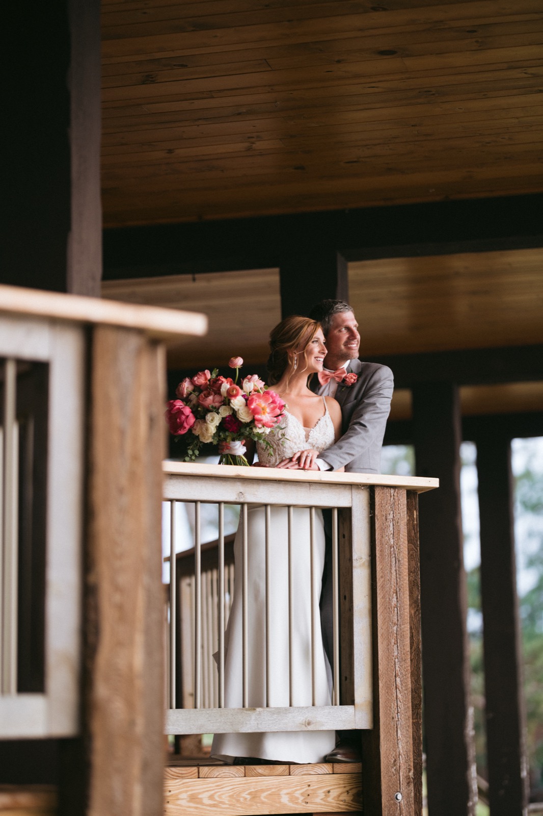 Melissa and Kody framed through a wooden porch railing at Madden's, both gazing out toward the open light beyond — Tim Larsen Photography, Brainerd Lakes MN